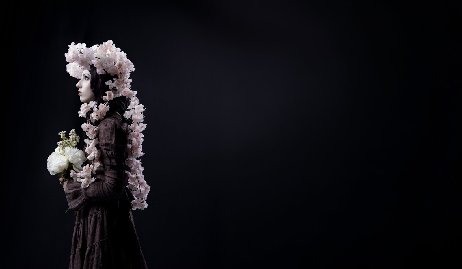 A woman in profile, crowned and draped in pale cherry blossoms, holding white peonies against black